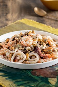 a white bowl filled with pasta and shrimp on top of a table next to a spoon