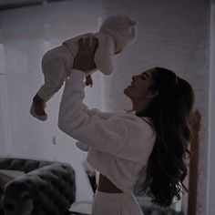 a woman holding a baby up to her face in the air while standing next to a couch