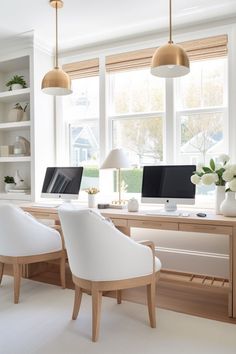 two white chairs in front of a desk with computer monitors on it and flowers near the window