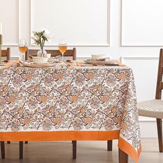 an orange and white table cloth on top of a dining room table with wine glasses