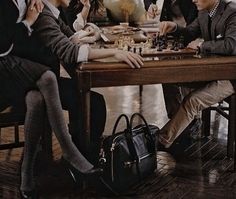 a group of people sitting around a wooden table playing chess with one person wearing a suit and tie