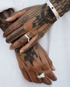 two tattooed hands holding each other with rings on their fingers and fingernails attached to them