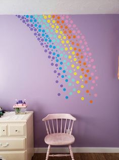 a chair in front of a purple wall with polka dots on it and a rainbow painted on the wall