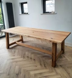 a large wooden table sitting on top of a hard wood floor next to two windows