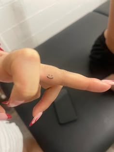 a woman's hand with a smiley face tattoo on her left thumb and finger