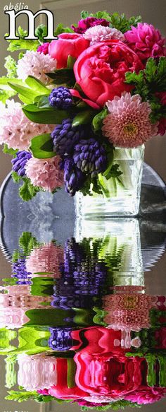 a vase filled with lots of flowers sitting on top of a table next to a mirror