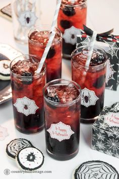 four glasses filled with red liquid on top of a white table covered in black and white decorations