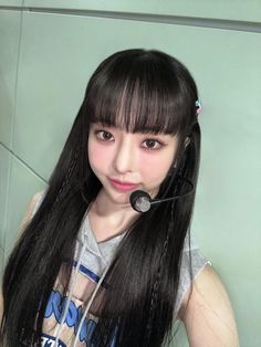 a girl with long black hair wearing a headset and looking at the camera while standing in front of a wall