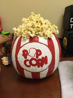 a red and white striped pumpkin with popcorn in it sitting on a table next to other items