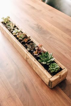 a wooden planter filled with lots of succulents on top of a table