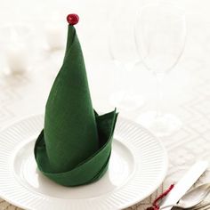 there is a small green paper christmas tree on the plate with silverware next to it