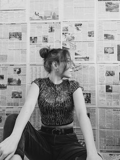 a woman sitting on the floor in front of a wall covered with newspaper pages and papers