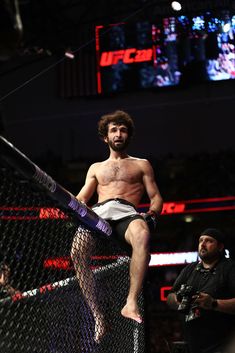 a man standing on top of a cage holding a baseball bat in his right hand