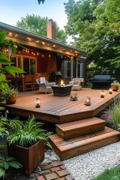 A cozy wooden deck with wicker chairs, a fire pit, string lights, and lanterns, surrounded by lush greenery and a brick patio with potted plants. Stone Patio Off Of Deck Ideas, Wood Deck And Stone Patio, Decks On Sloped Backyards, Ground Level Deck Ideas With Pergola, Long Back Deck Ideas, Ranch Home Deck Ideas, Backyard Deck Lighting, Backyard Deck Inspiration, Freestanding Deck Ideas