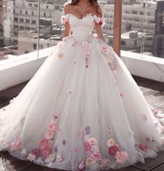 a woman in a white wedding dress with flowers on the skirt and off the shoulder