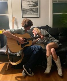 a man and woman sitting on a couch playing guitar