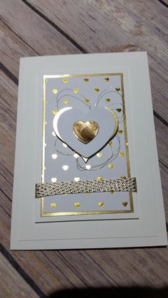 a white card with gold foil on it and a heart in the middle, sitting on top of a wooden table