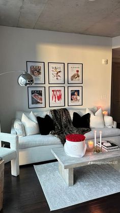 a living room filled with white furniture and pictures on the wall above it's coffee table