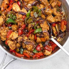 a pan filled with chicken and peppers on top of a white counter next to a spoon