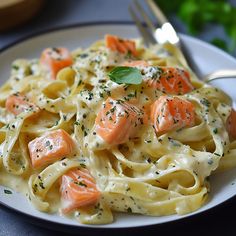 a white plate topped with pasta covered in salmon and cheese sauce next to a fork