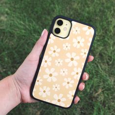 a person holding an iphone case with flowers on it in their hand and grass behind them