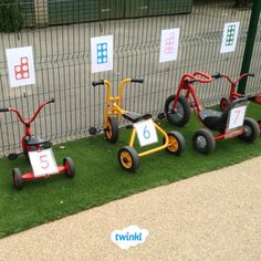 several tricycles are lined up on the grass in front of a fenced area