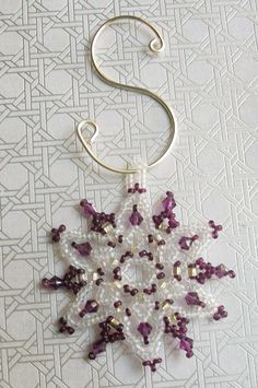 a beaded snowflake hanging from a hook on a white wallpaper background