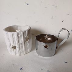 two silver mugs sitting next to each other on a white tablecloth covered surface