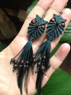 a pair of earrings with beads and feathers on the palm tree branch in someone's hand