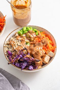 a bowl filled with rice, meat and vegetables next to a container full of sauce