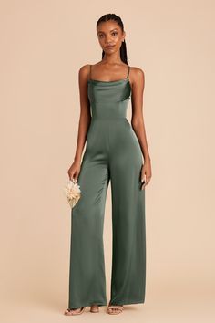 a woman wearing a green jumpsuit with spaghetti straps and wide legs, standing in front of