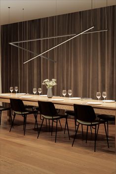 a long table with chairs and wine glasses on it in front of a curtained wall