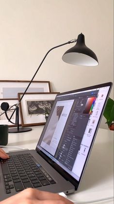 a person using a laptop computer on a white desk in front of a black lamp