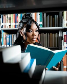 a woman reading a book in front of a bookshelf