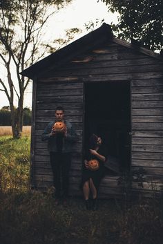 two people standing in the doorway of an outhouse with pumpkins on their hands