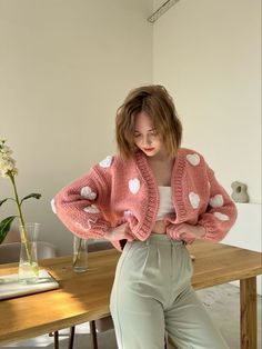 a woman sitting at a table with her hands on her hips wearing a pink cardigan