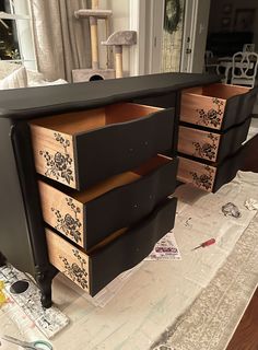 an old dresser is painted black and has floral designs on the drawer fronts, along with other pieces of furniture