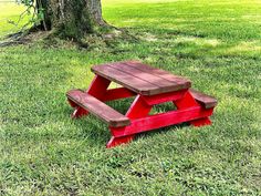 a red picnic table sitting in the grass under a tree