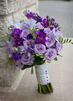 a bouquet of purple flowers sitting next to a stone wall