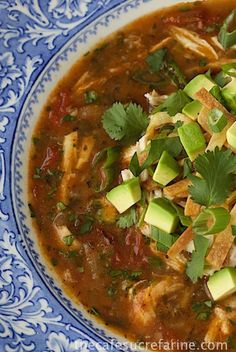 a blue and white bowl filled with soup topped with avocado slices, cilantro and sour cream