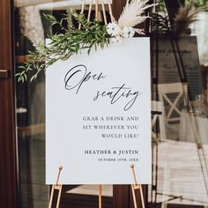 a sign that is on top of a easel in front of a door with flowers and greenery