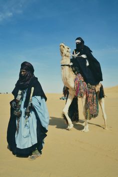 two people riding on top of a camel in the desert