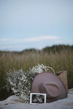 a hat and flowers on a blanket in the middle of a field with a photo frame next to it