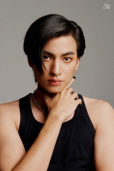 a young man with black hair and piercings posing for a photo in front of a gray background