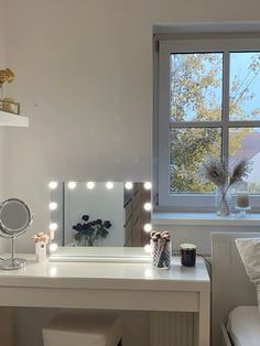 a white vanity with lights on it next to a mirror and chair in front of a window