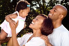 a man, woman and child smiling at each other with trees in the back ground