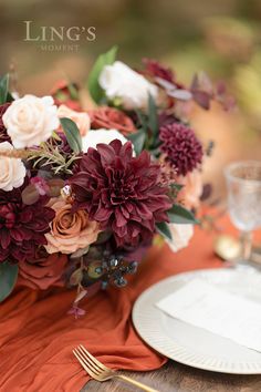 a bouquet of flowers is sitting on top of an orange table cloth with silverware