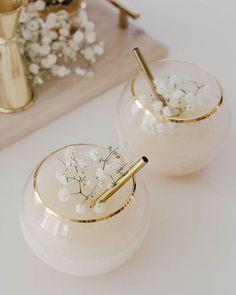 two white vases with flowers in them on top of a table next to a phone