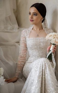 a woman in a wedding dress sitting on a couch holding a bouquet of white flowers