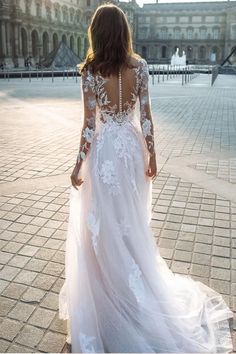 a woman in a white wedding dress is walking down the street with her back to the camera